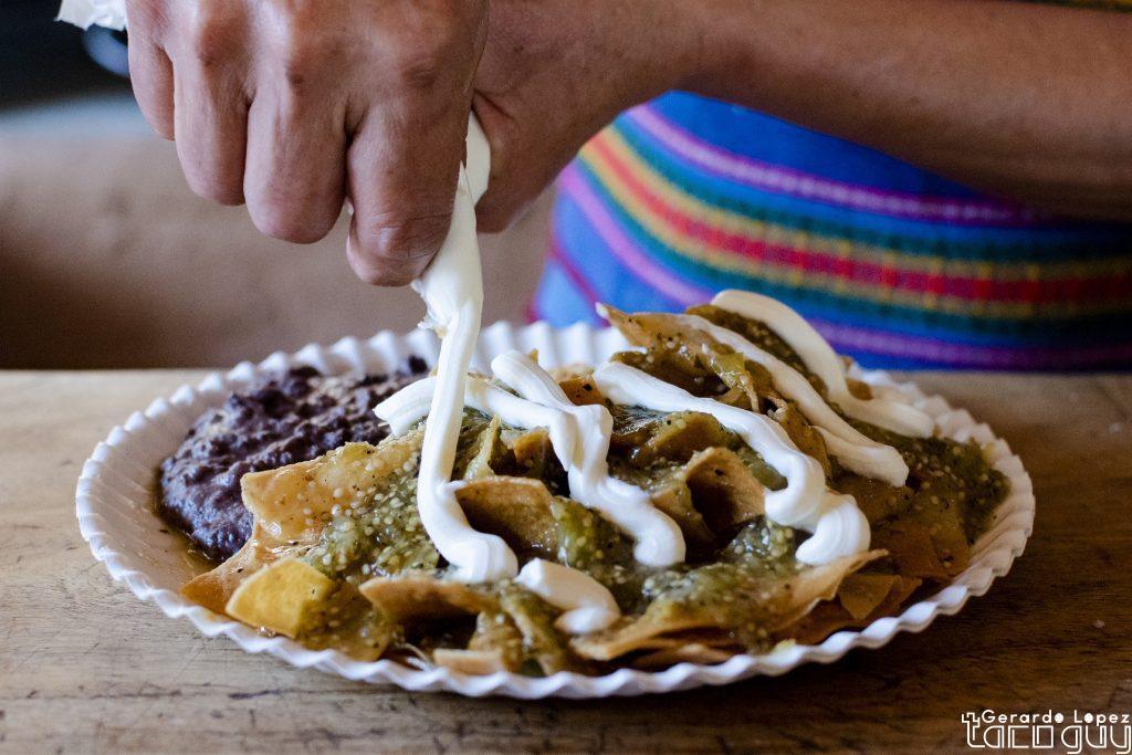Green Chilaquiles being garnished with crema on top